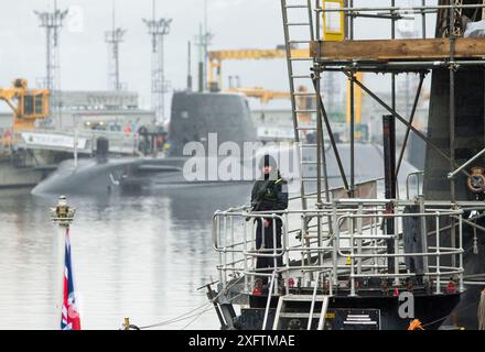 Aktenfoto vom 01/16 von einem Mitglied der bewaffneten Streitkräfte an Deck des U-Bootes der Vanguard-Klasse HMS Vigilant, eines der vier U-Boote mit Atomsprengkopf, mit dem U-Boot der Astute-Klasse HMS Artful dahinter auf der HM Naval Base Clyde, auch bekannt als Faslane. Innerhalb weniger Stunden nach dem Betreten der Downing Street wird Sir Keir Starmer mit der wahrscheinlich abschreckendsten seiner neuen Verantwortung konfrontiert sein - zu entscheiden, was passieren sollte, wenn Großbritannien durch einen Atomangriff ausgelöscht wird. Ausgabedatum: Freitag, 5. Juli 2024. Stockfoto