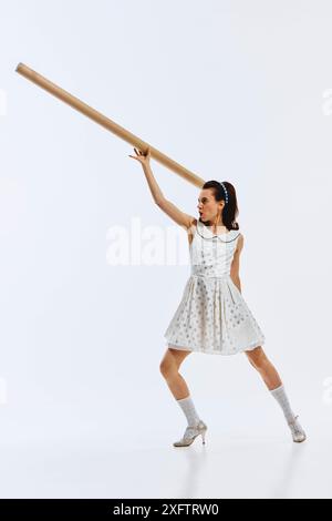 In einem Pünktchenkleid zeigt eine Frau mit einem Papprohr eine dynamische Pose und zeigt motivierte Emotionen. Neuer Start, Anfang, Start Stockfoto