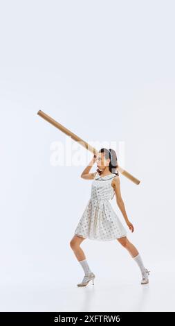 Die junge Frau im Pünktchenkleid und Vintage-Schuhen posiert spielerisch mit langen Pappröhrchen. Klassischer Stil der 1950er Jahre. Entschlossene und motivierte Mitarbeiter Stockfoto