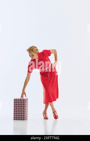 In einem leuchtenden roten Kleid mit Punktmuster posiert eine Frau mit einem gewickelten Geschenk auf weißem Hintergrund. Urlaubsstimmung. Stockfoto