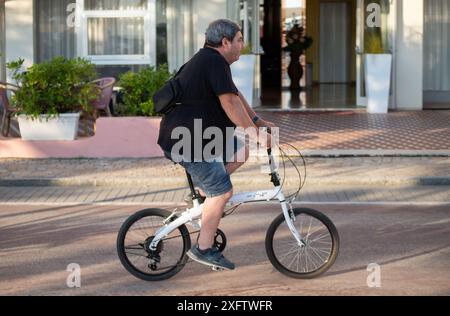 Übergewichtiger Mann, der in humorvoller Szene mit kleinem Fahrrad fährt Stockfoto