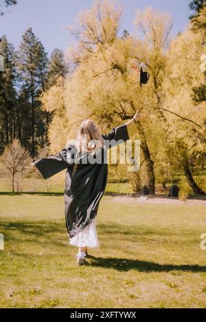 Absolvent wirft Mütze in die Luft, feiert in einem sonnigen Park Stockfoto