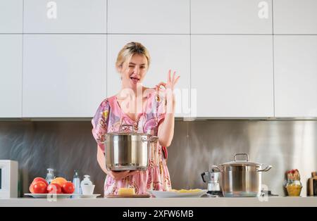 Eine Frau mit Kochtopf steht neben dem Tisch in der Küche zu Hause. Die Hausfrau kocht morgens in der Küche. Stockfoto