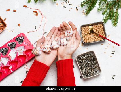 Schritt 7: Blick von oben auf Kinderhände mit einem herzförmigen hausgemachten Vogelsamenkuchen aus Vogelsamen, Nüssen und Kokosfett. Helfen Sie Menschen bei Tieren. Stockfoto