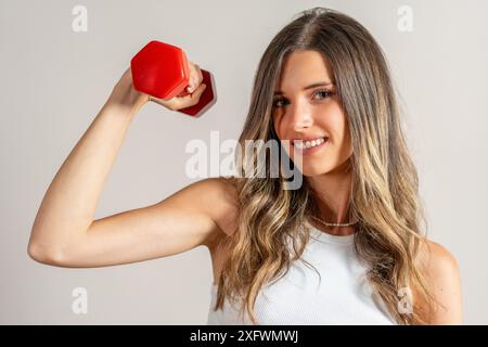 Frau, die eine rote Hantel hebt - Schwerpunkt auf Krafttraining - gesunde Übungsroutine, Fitness-Motivation - Gym Hintergrund. Stockfoto