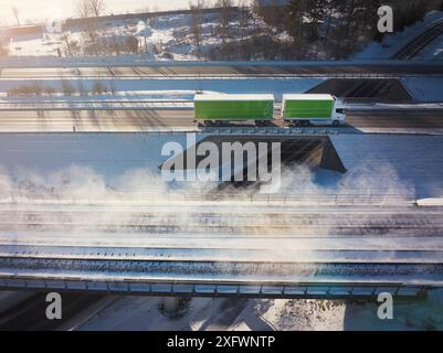 Drohnenansicht des Lkws auf der Überführung von Eisenbahngleisen inmitten von Schnee Stockfoto