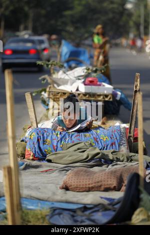 Ein Teenager aus einer obdachlosen Familie lernt am besten an einem sonnigen Wintermorgen, um ein Bett auf einem Straßenteiler zu bekommen. Das Foto stammt von Palashi Ar Stockfoto