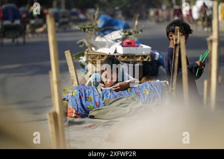 Ein Teenager aus einer obdachlosen Familie lernt am besten an einem sonnigen Wintermorgen, um ein Bett auf einem Straßenteiler zu bekommen. Das Foto stammt von Palashi Ar Stockfoto