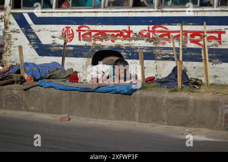 Ein Teenager aus einer obdachlosen Familie lernt am besten an einem sonnigen Wintermorgen, um ein Bett auf einem Straßenteiler zu bekommen. Das Foto stammt von Palashi Ar Stockfoto