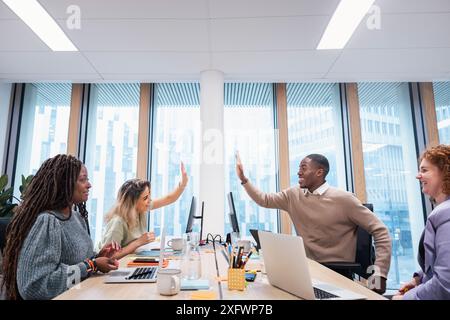 Glücklicher Geschäftsmann und Geschäftsfrau geben High-Five, während er mit Kollegen im Büro arbeitet Stockfoto