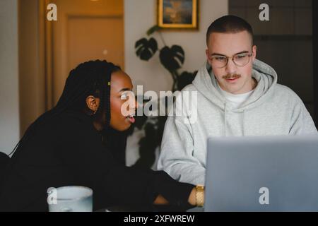 Fokussierte multirassische männliche und weibliche Kollegen diskutieren, während sie zu Hause am Laptop arbeiten Stockfoto
