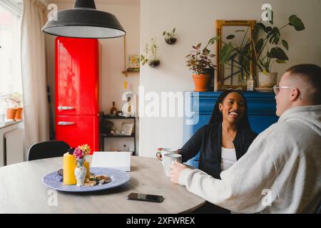Glückliche Paare, die miteinander reden, während sie zu Hause einen Kaffee trinken Stockfoto