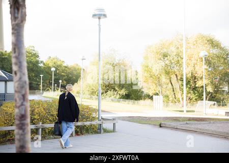 Rückansicht eines Teenager-Mädchens, das am sonnigen Tag auf dem Gehweg läuft Stockfoto