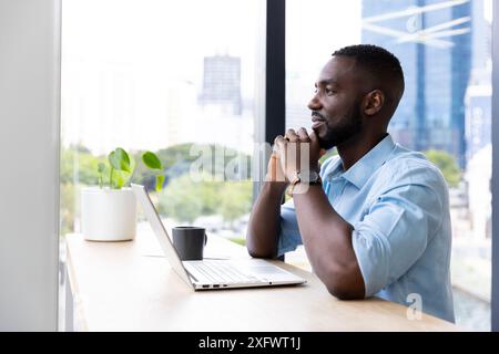 Tief nachdenkend, Mann sitzt am Schreibtisch mit Laptop und Kaffee im Büro Stockfoto