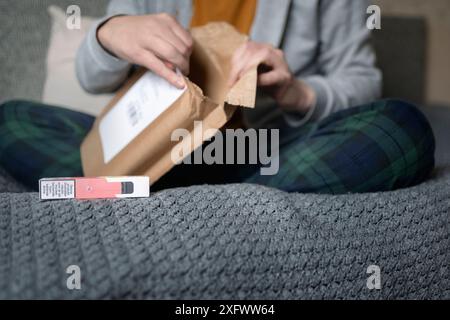 Mittelteil des Mannes, der das Paket mit Vape Pen öffnet, während er auf dem Bett sitzt Stockfoto