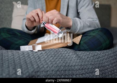 Der Mittelteil des Mannes zerreißt ein Paket mit einem Vape Pen, während er auf dem Bett sitzt Stockfoto