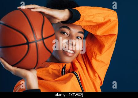 Nahaufnahme einer jungen Frau in orangener Sportbekleidung, die Basketball hält. Porträt einer Basketballspielerin, die im Studio in die Kamera schaut. Stockfoto