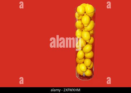 Eine transparente Glasvase gefüllt mit frischen, Reifen, gelben Zitronen steht auf einem roten Stoffhintergrund. Stockfoto