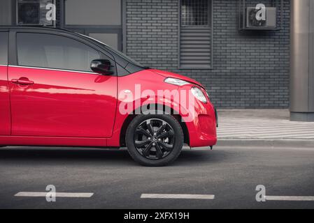 Nahaufnahme des roten Citroen C1: Vorderer Stoßfänger und Scheinwerfer im Fokus und dunkelgraue Wand im Hintergrund. Stockfoto