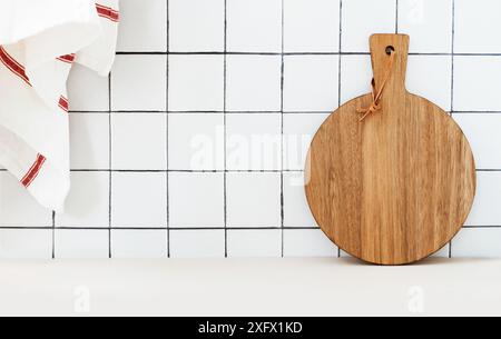 Stilvoller weißer Küchenhintergrund mit Küchentuch und hölzernem Schneidebrett, die auf weißer Arbeitsplatte stehen, Kopierraum für Text, Vorderansicht Stockfoto