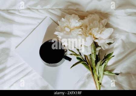 Strauß von weißen Pfingstrosenblüten, Magazin, Tasse Tee auf weißem schlechtem Textil. Draufsicht. Kopierbereich Stockfoto