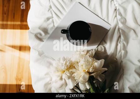 Strauß von weißen Pfingstrosenblüten, Magazin, Tasse Tee auf weiß schlecht im Sonnenlicht. Draufsicht. Kopierbereich Stockfoto