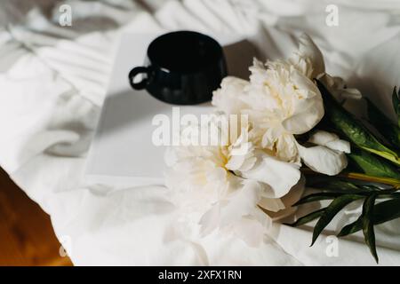 Strauß von weißen Pfingstrosenblüten, Magazin, Tasse Tee auf weiß schlecht im Sonnenlicht. Draufsicht. Kopierbereich Stockfoto