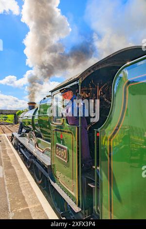 Eine Dame „Feuerwehrmann“ auf der erhaltenen ehemaligen GWR-Lok 6990 „Witherslack Hall“, die den Bahnhof Williton an der West Somerset Railway, England, Vereinigtes Königreich, verlässt Stockfoto