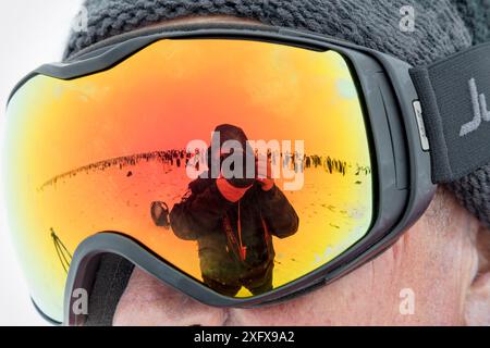 Die Fotografin Sue Flood fotografiert sich selbst und die Kolonie des Kaiserpinguins (Aptenodytes forsteri) als Spiegelbild einer Brille, Gould Bay, Weddell Sea, Antarktis. Stockfoto