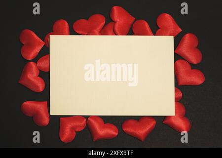 Horizontales Foto einer Valentinskarte, umgeben von kleinen Stoffherzen. Flaches Foto auf schwarzem Hintergrund mit Textabstand. Stockfoto