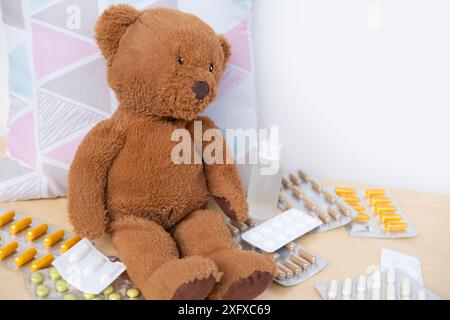 teddybär krank, umgeben von verstreuten Medikamenten und Pillen, Gesundheit, Pflege und Behandlung Kinder durch Kuschelspielzeug, medizinische Therapie und Pädiatrie Stockfoto