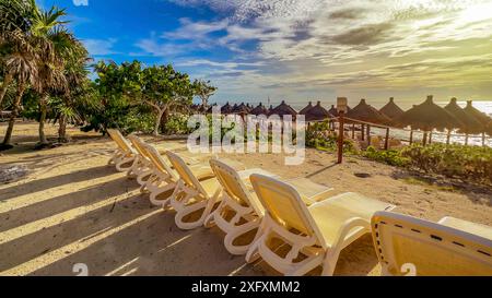 Panoramablick auf eine tropische Landschaft und Landschaft mit Liegestühlen und Strohschirmen an einem Strand aus feinem weißem und goldenem Sand, unter blauem Himmel und Stockfoto