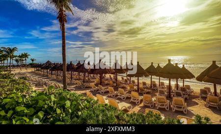 Panoramablick auf eine tropische Landschaft und Landschaft mit Liegestühlen und Strohschirmen an einem Strand aus feinem weißem und goldenem Sand, unter blauem Himmel und Stockfoto