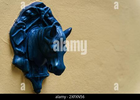 Sevilla, Spanien. 8. Februar 2024 - kleine blaue Pferdekopfskulptur auf gelber Wand, Nahaufnahme Stockfoto