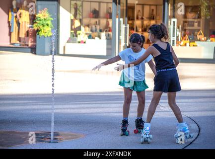 Zwei Mädchen auf Rollschuhen, die im Springbrunnen spielen. Stockfoto