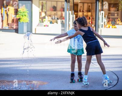 Zwei Mädchen auf Rollschuhen, die im Springbrunnen spielen. Stockfoto