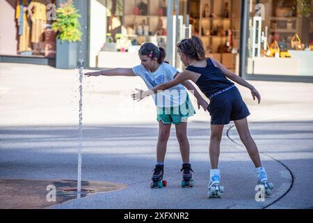 Zwei Mädchen auf Rollschuhen, die im Springbrunnen spielen. Stockfoto