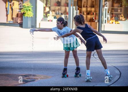 Zwei Mädchen auf Rollschuhen, die im Springbrunnen spielen. Stockfoto