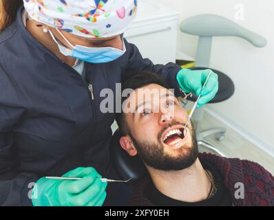 Eine Zahnärztin untersucht einen männlichen Patienten in einer Zahnarztpraxis mit professionellen Werkzeugen und persönlicher Schutzausrüstung. Stockfoto