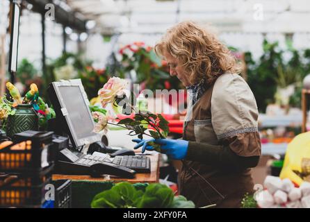 Blumengeschäft mit professionellen Kleidung in einer Baumschule. Konzept der elektronischen Bestellung und Zahlung. Stockfoto