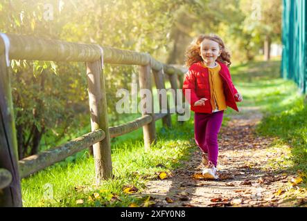 Adorable kleine Mädchen walking im Park auf einen Tag fallen. Weibliche Toddler mit gelb, rot und lila Kleidung. Stockfoto