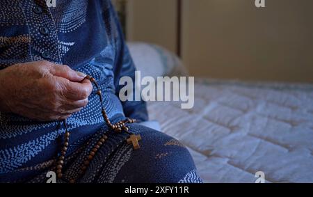 Ältere Frau 70-80 Jahre alt betet mit dem Rosenkranz zu Hause. Stockfoto