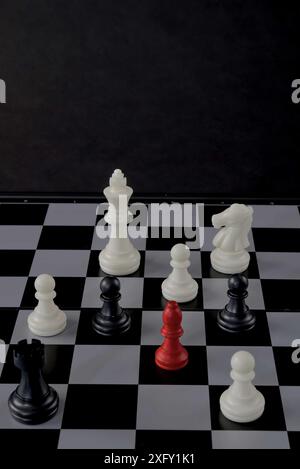 Ein Schachbrett mit einem roten Bauern, umgeben von schwarz-weißen Schachfiguren. Fremder, Außenseiter, anders, Sonstiges, Stockfoto