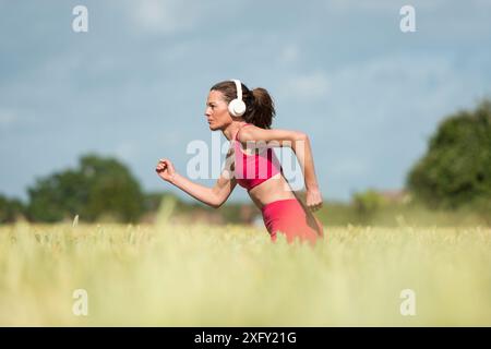 Sportliche Läuferin, die durch das Land läuft, Weizenfeld. Stockfoto