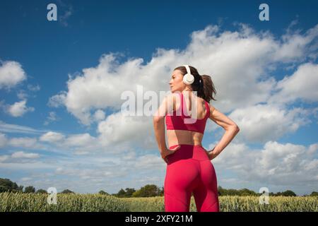 Sportliche Frau mit Kopfhörern, draußen mit blauem Himmel Hintergrund, Rückansicht. Stockfoto