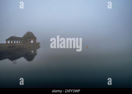 Dammauer am Edersee im Morgennebel, Reflexion im ruhigen Wasser. Bezirk Waldeck-Frankenberg, Hessen, Deutschland. Stockfoto