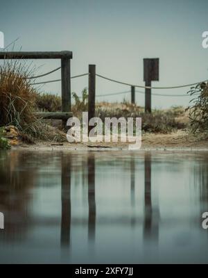 Holzzaun-Pfosten spiegeln sich in einer Küsten-Puddle an einem bewölkten Tag Stockfoto