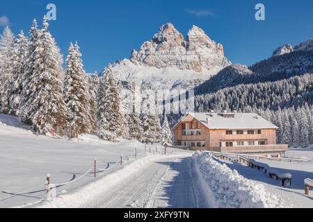 Italien, Veneto, Provinz Belluno, Auronzo di Cadore, Dolomiten - schneebedeckte Straße und Unterkunft für Touristen in Misurina, Winterpanorama mit dem berühmten Tre Cime di Lavaredo im Hintergrund Stockfoto