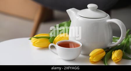 Tasse heißer Tee, Tulpen und Teekanne auf dem Tisch im Zimmer Stockfoto