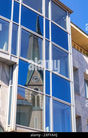 Der Glockenturm der Nikolaikirche spiegelt sich in den Glasfenstern des modernen Gebäudes in der Nähe des Kongresszentrums in Villach, Kärnten, Österreich Stockfoto